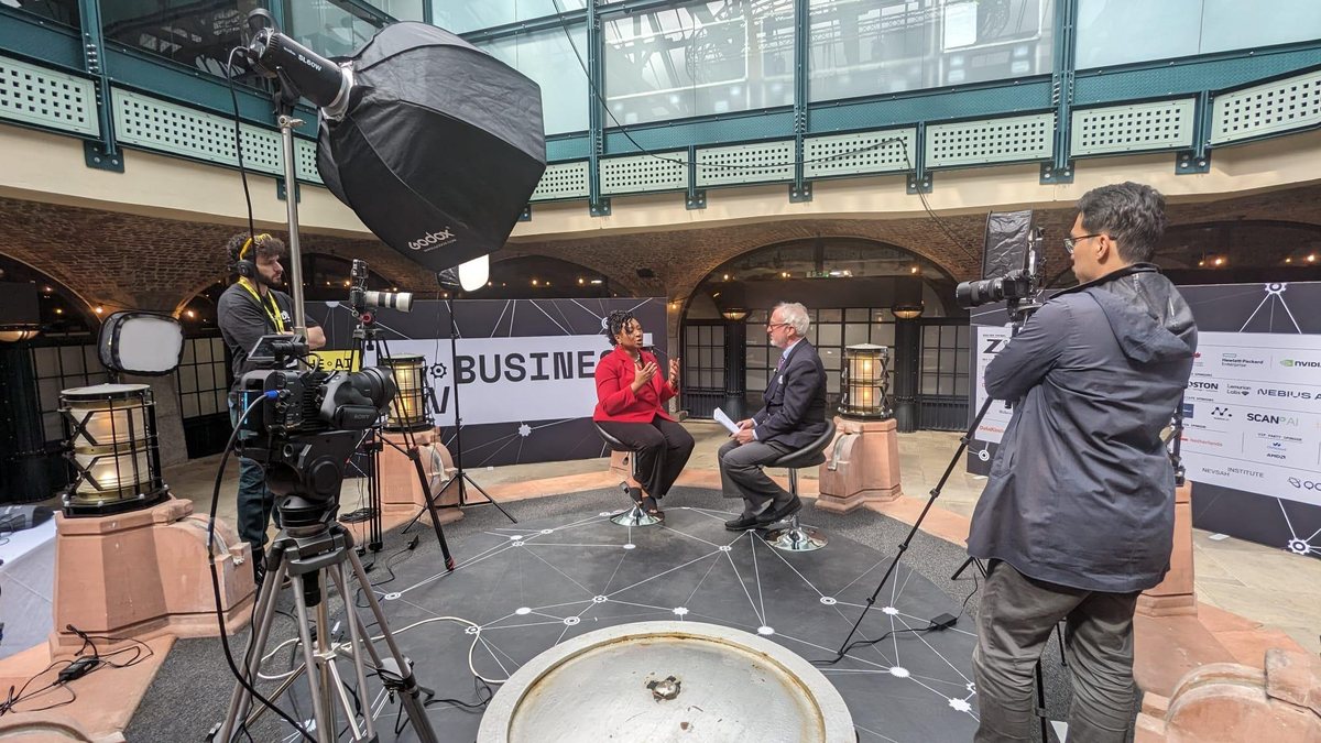 Camera crew filming a seated interview under a glass roof in a market hall