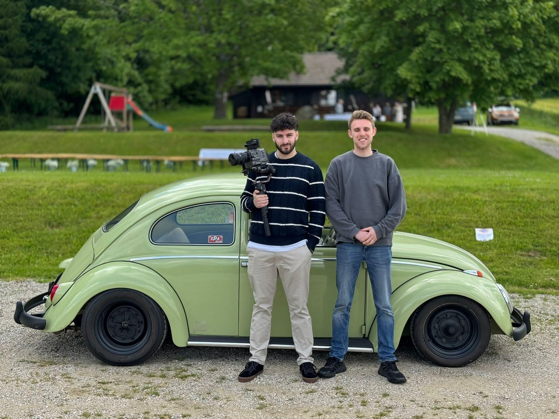 Ben and Hadrien standing beside a pale green Volkswagen Beetle, one holding a camera rig
