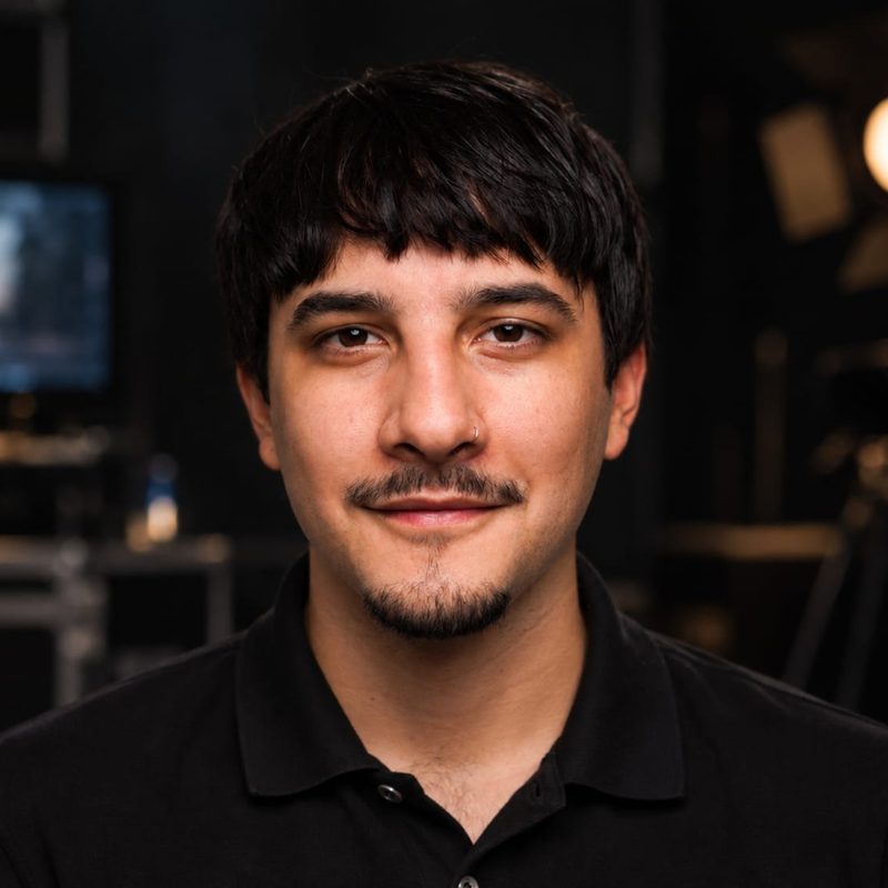 Emanuel in a black polo shirt in front of an edit suite and a studio light