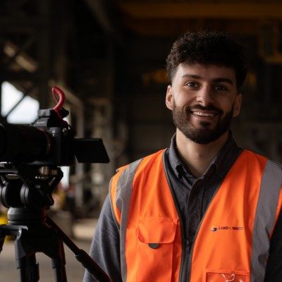 Hadrien Torres smiling in a hi-vis vest beside a camera on a tripod