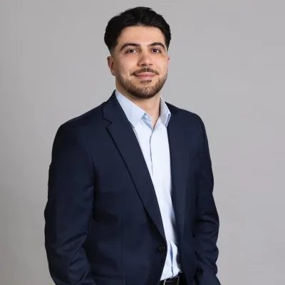 Koray in a navy suit against a grey wall