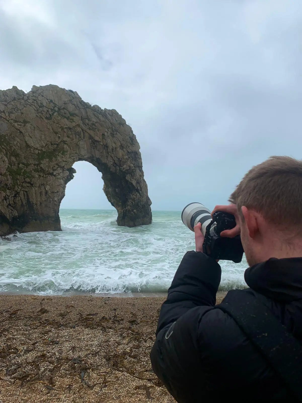 Photographer shooting the Durdle Door rock arch from the beach